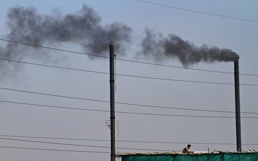 Un Indien travaille sur le toit d'une usine alors que la fumée monte d'une autre usine dans une zone industrielle d'Ahmadabad
