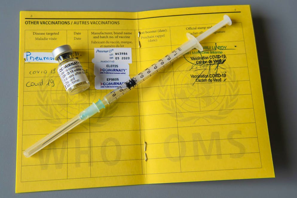 Une fiole du vaccin Pfizer-BioNTech et une seringue sont photographiees sur un carnet de l'OMS de certificat international de vaccination ou de prophylaxie, faudra-t-il un jour un passeport vaccinal, afin d'etre libre et ainsi prouver qu'une personne a bien ete vaccinee contre le virus et de pouvoir ainsi voyager de prendre l'avion, d'aller dans une salle de Cinema ou un restaurant ou dans un autre pays, lors du dernier jour de vaccination dans les EMS du Canton de Vaud pendant la pandemie de Coronavirus Covid-19, ce jeudi, 18 mars 2021 a Nyon. (KEYSTONE/Martial Trezzini)