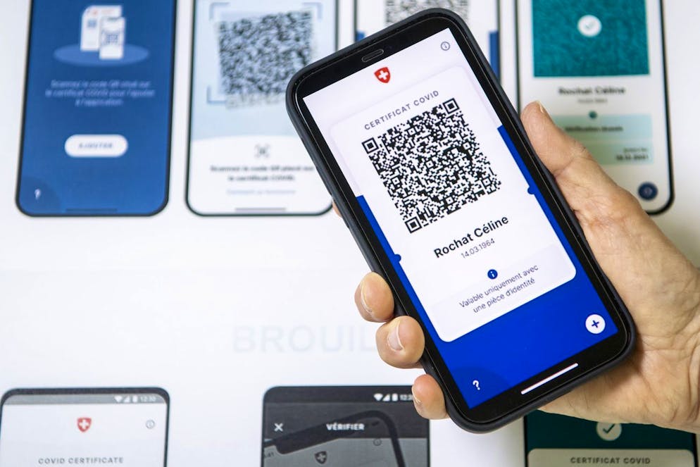 Un smartphone est visible a cote d'un visuel presentant un specimen de l'aspect du nouveau certificat Covid le vendredi 4 juin 2021 a Lausanne. Le Conseil federal presente aujourd'hui en conference de presse les details du certificat Covid. (KEYSTONE/Jean-Christophe Bott)