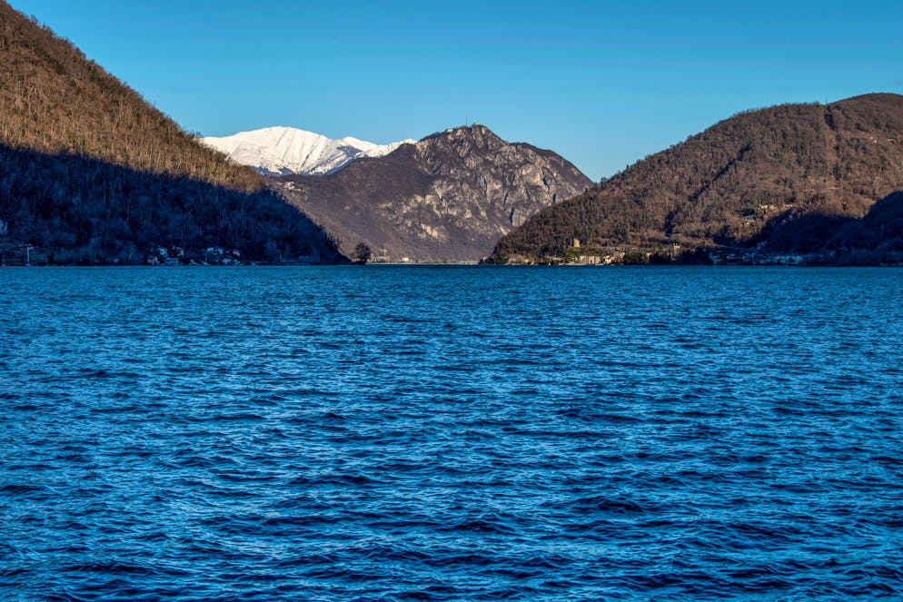 Luganese: turismo invernale, paesaggi invernali. Nella foto sullo sfondo montagne innevate nel luganese, prime luci sul Monte San Salvatore. In ombra golfo lago Ceresio, Lugano. © Ti-Press / Francesca Agosta