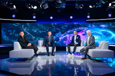 Vier Sportexperten sitzen in einem Fernsehstudio für Sportübertragungen auf weißen Sofas vor einem großen Bildschirm mit Champions-League-Motiv.