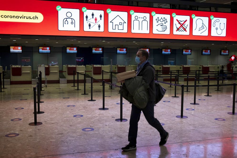 Passenger wearing a face mask passes in front of a information screen with advice on how to fight against the spread of coronavirus COVID-19 in the almost empty check-in hall at the Geneva Airport (Geneve Aeroport) during the coronavirus disease (COVID-19) outbreak, in Geneva, Switzerland, Tuesday, November 10, 2020. Switzerland as many countries in Europe impose more coronavirus restrictions as cases of Covid-19 patients spike in a second wave of pandemic. (KEYSTONE/Laurent Gillieron)