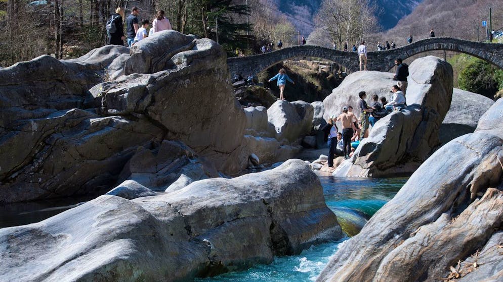 Osterausfluegler geniessen am Sonntag, 4. April 2021, trotz der Maskenpflicht im Freien das schoene Wetter am Ponte dei Salti ueber den Fluss Verzasca bei Lavertezzo. Am Ponte dei Salti und den angrenzenden Gebieten gilt wegen der grassierenden Corona-Pandemie die allgemeine Maskenpflicht. Auch andere von Touristen und Ausflueglern stark frequentierte Orte im Tessin haben vor Ostern die Maskenplicht im Freien eingefuehrt. (KEYSTONE/Ti-Press/Alessandro Crinari)