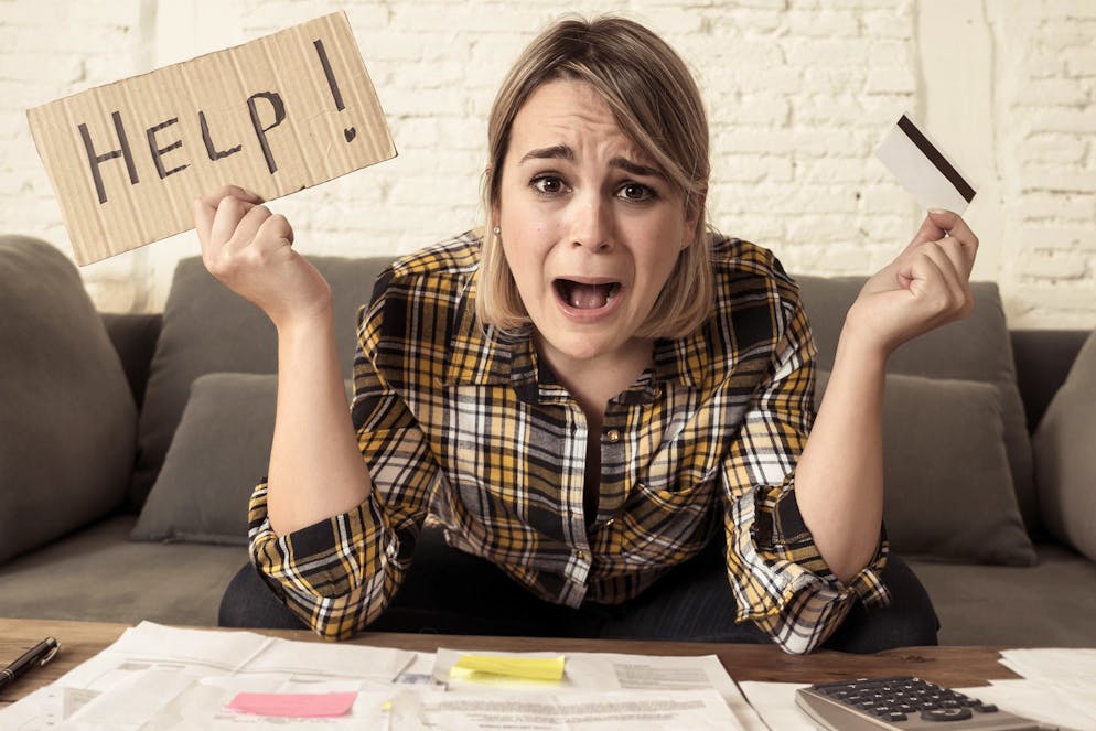 Portrait of worried young woman feeling stressed with too much credit card debts trying to manage business and home finances showing Help sign. In paying off debts, bills and financial problems.