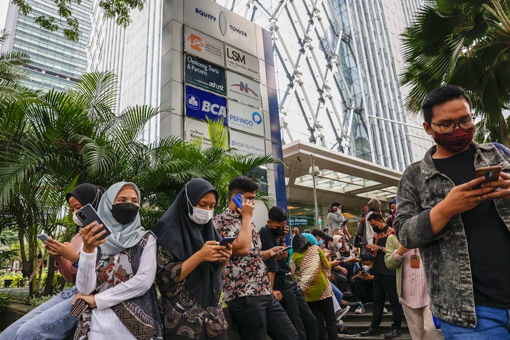 Les employés de bureau vérifient leurs téléphones pendant qu'ils attendent à l'extérieur d'une tour de bureaux au milieu des craintes de répliques à la suite d'un tremblement de terre dans un quartier d'affaires de Jakarta, Indonésie, le 14 janvier 2022.