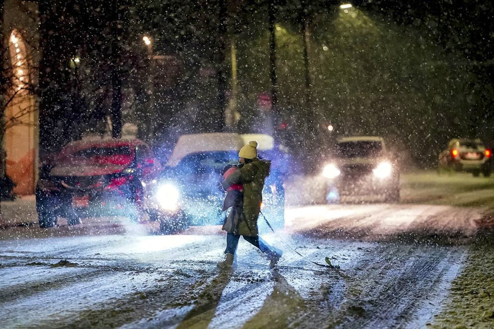 Une personne porte son chien alors qu'elle traverse Butler Street alors que la neige tombe lors d'une tempête hivernale qui touchera la région dimanche soir 16 janvier 2022, dans un quartier de Lawrenceville à Pittsburgh.