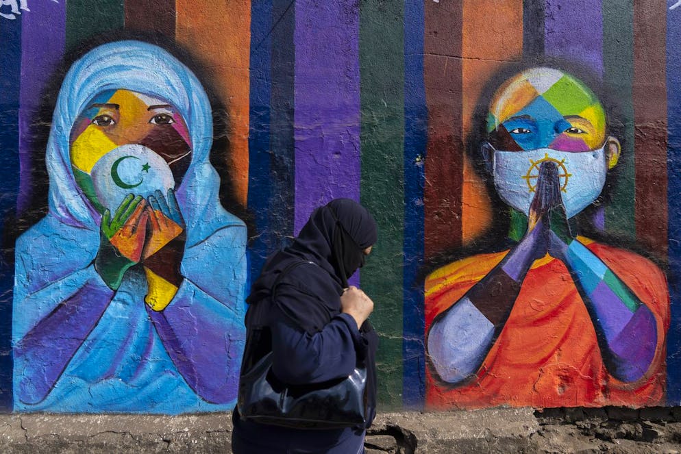 A woman walks past a graffiti painted on a wall to create awareness coronavirus disease, in Mumbai, India, Thursday, Feb. 3, 2022. (AP Photo/Rafiq Maqbool)