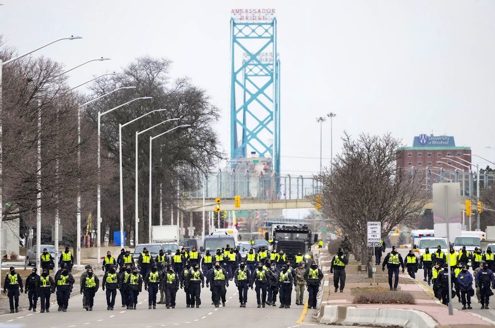 Police walk the line to remove truckers and supporters after a court injunction gave police the power to enforce the law after protesters blocked the access leading from the Ambassador Bridge, linking Detroit and Windsor, as truckers and their supporters continue to protest against COVID-19 vaccine mandates and restrictions in Windsor, Ontario, Sunday, Feb. 13, 2022. (Nathan Denette/The Canadian Press via AP)
