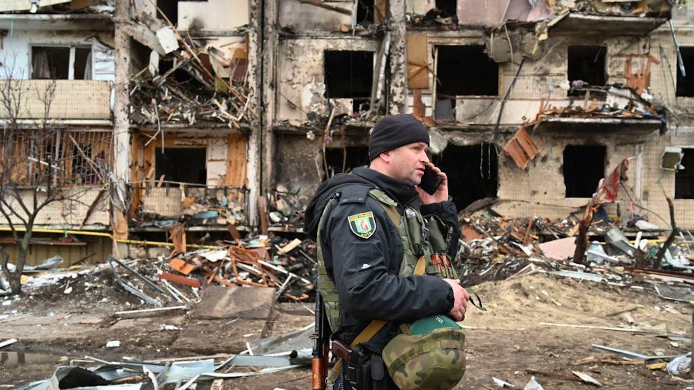 A police officer stands guard at a damaged residential building at Koshytsa Street, a suburb of the Ukrainian capital Kyiv, where a military shell allegedly hit, on February 25, 2022. - Invading Russian forces pressed deep into Ukraine as deadly battles reached the outskirts of Kyiv, with explosions heard in the capital early Friday that the besieged government described as