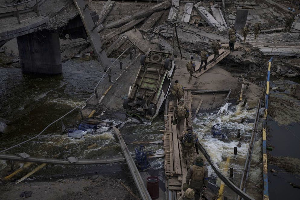 Foreign and Ukrainian soldiers cross an improvised path under a destroyed bridge in Irpin, outskirts of Kyiv, Ukraine, Saturday, March 12, 2022. Kyiv northwest suburbs such as Irpin and Bucha have been enduring Russian shellfire and bombardments for over a week prompting residents to leave their homes. (AP Photo/Felipe Dana)
