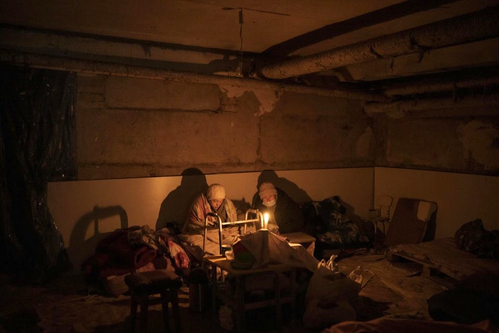 Two elderly woman lit by a candle hide in a basement used as a bomb shelter in Irpin, outskirts of Kyiv, Ukraine, Sunday, March 13, 2022. (AP Photo/Felipe Dana)