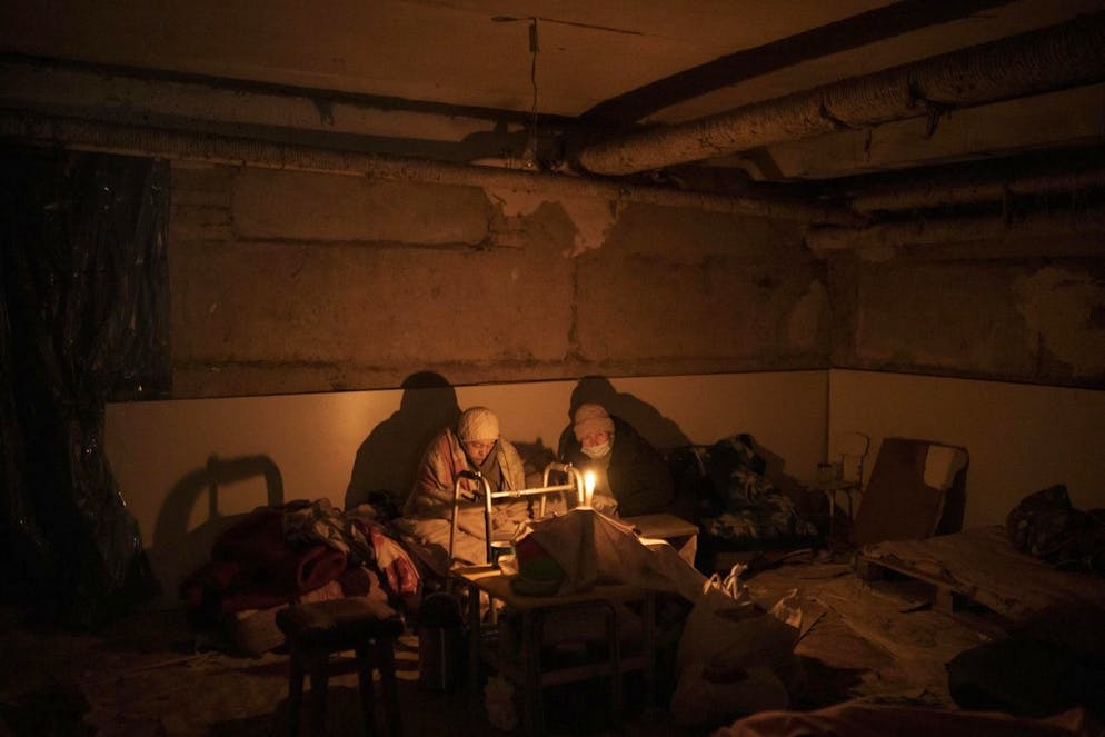 Two elderly woman lit by a candle hide in a basement used as a bomb shelter in Irpin, outskirts of Kyiv, Ukraine, Sunday, March 13, 2022. (AP Photo/Felipe Dana)