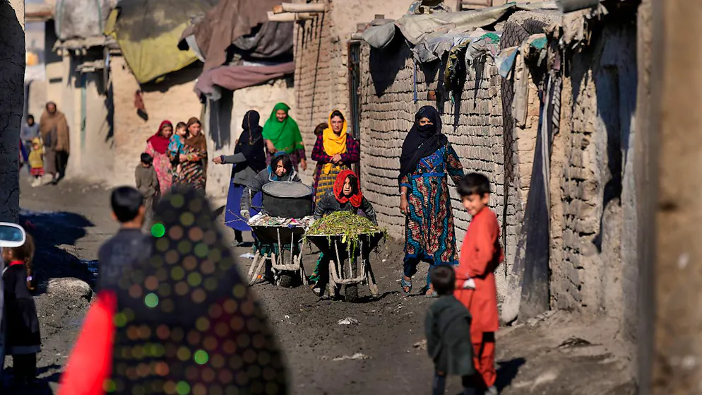Frauen und Kinder schieben Schubkarren und gehen eine schlammige Gasse in einem Armutsviertel von Kabul entlang.