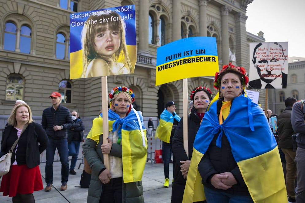 Protesters wear Ukrainian flags and hold banners during a demonstration against the Russian invasion of Ukraine in front of the Swiss parliament building in Bern, Switzerland, Saturday, March 19, 2022. (KEYSTONE/Peter Klaunzer)