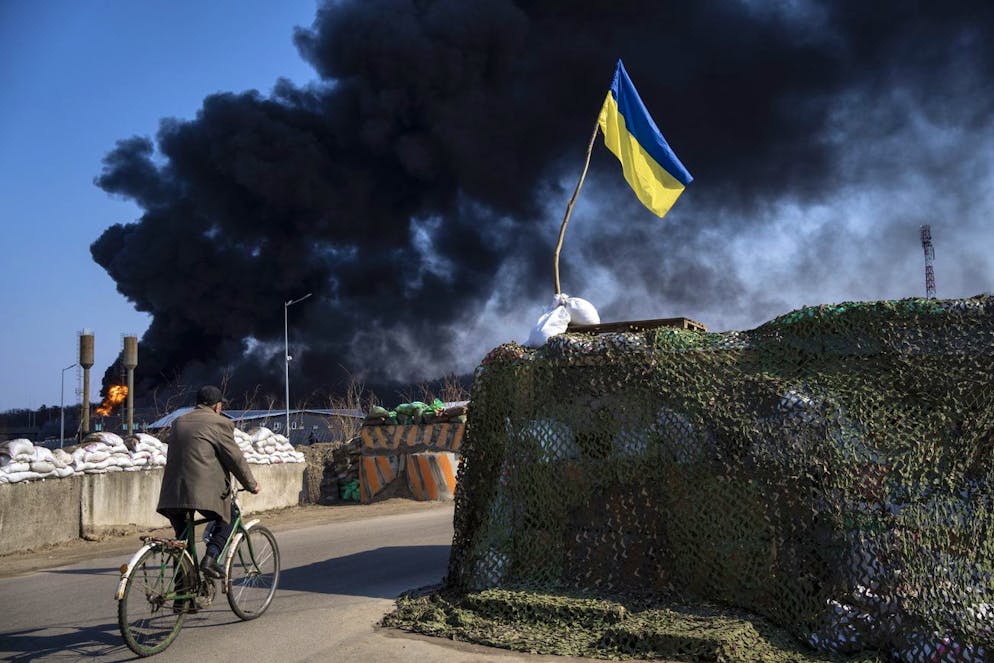 A man rides a bicycle as black smoke rises from a fuel storage of the Ukrainian army following a Russian attack, on the outskirts of Kyiv, Ukraine, Friday, March 25, 2022. (AP Photo/ (AP Photo/Rodrigo Abd)