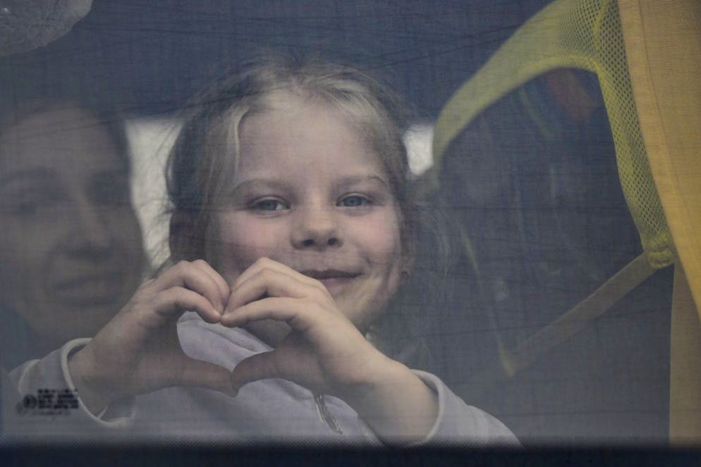 A child fleeing the war from neighbouring Ukraine with her family makes a heart shape with her hands as she looks out the window of a bus after crossing the border by ferry at the Isaccea-Orlivka border crossing, in Romania, Friday, March 25, 2022. (AP Photo/Andreea Alexandru)