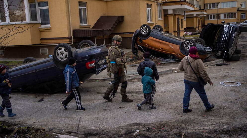 Ein ukrainischer Soldat geht in Butscha mit Kindern an zerstörten Autos vorbei.