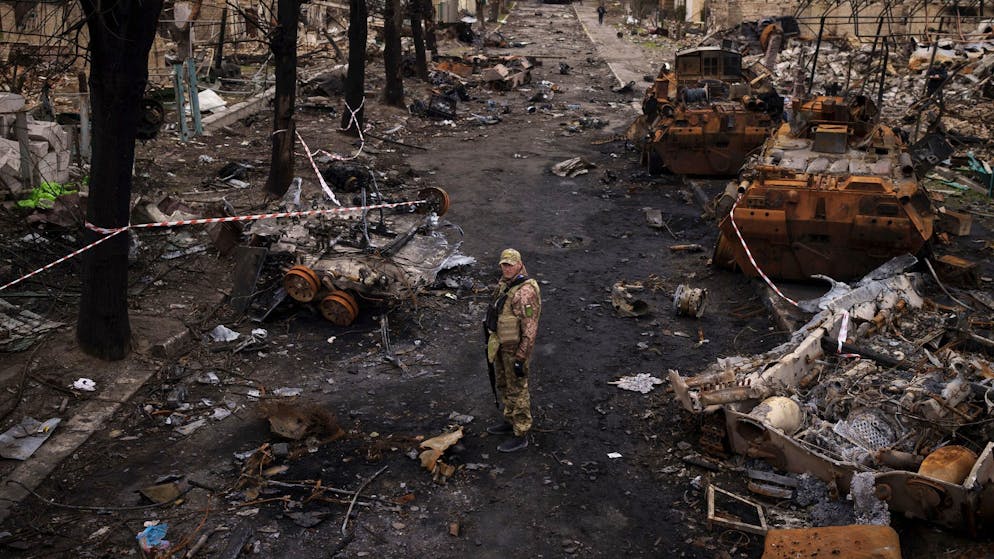 Ein ukrainischer Soldat steht in Butscha neben zerstörten russischen Panzern.