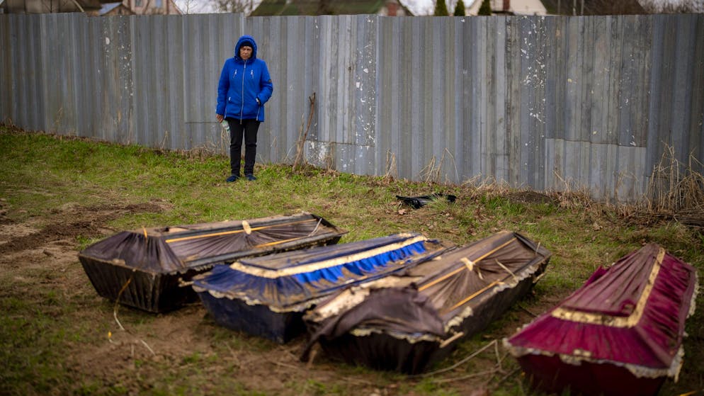 Eine Frau steht während der Exhumierung eines Massengrabes neben Särgen in Butscha.