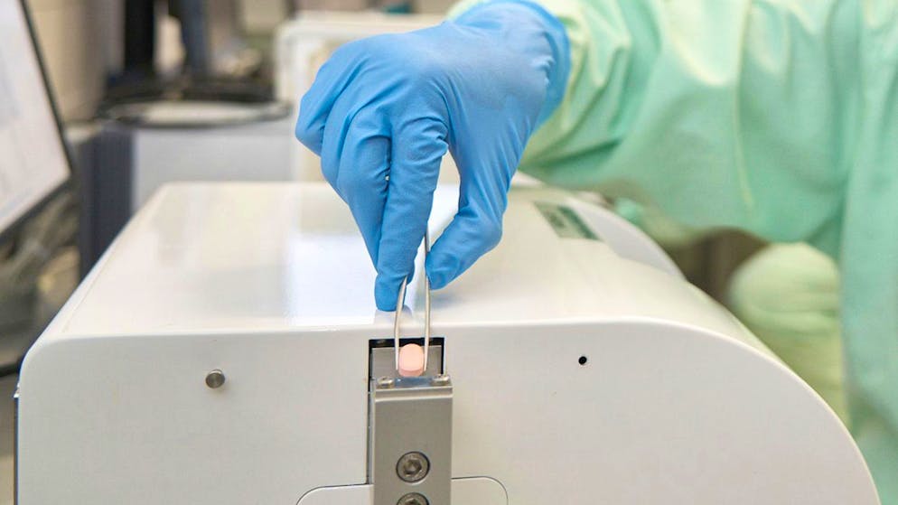 Ein Vorteil vom Corona-Medikament Paxlovid ist seine Tablettenform. Ein Pfizer-Labortechniker untersucht eine Paxlovid-Tablette auf die Wirkung von Druck. 