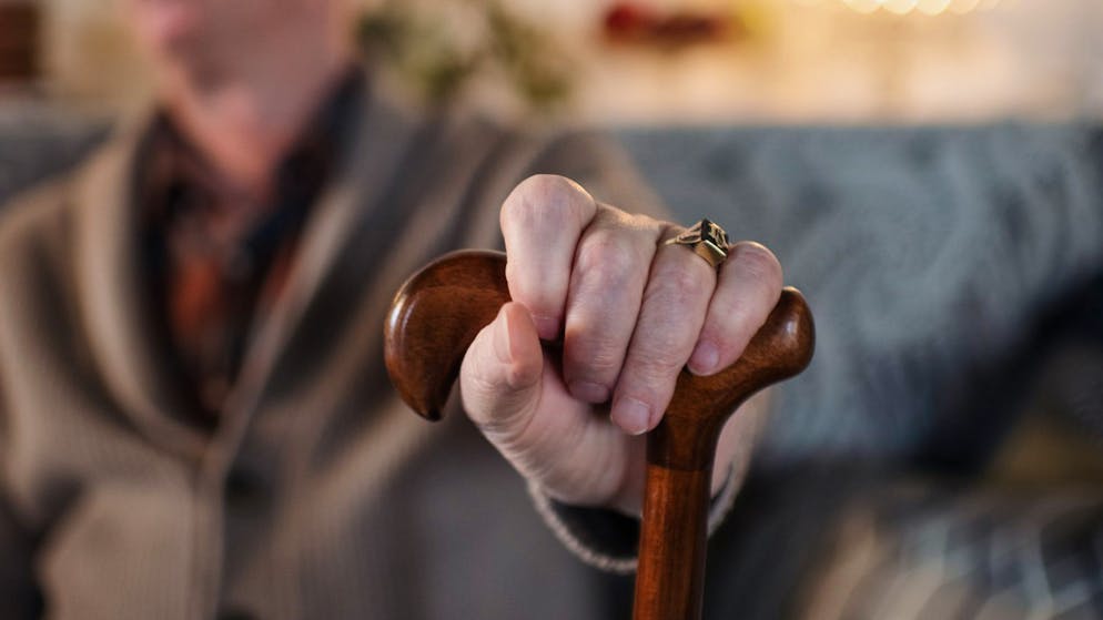 Happy old man with walking stick sitting on sofa, detail on hand.