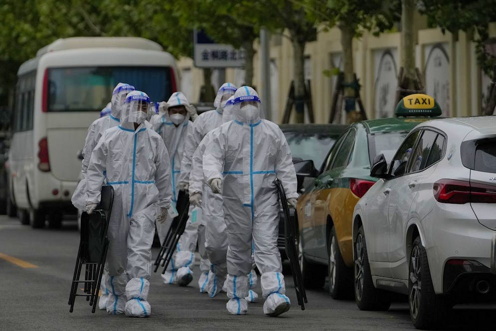Workers in protective suits carry foldable chairs as they head to a locked-down residential complex on Sunday, May 8, 2022, in Beijing. China is staying with a