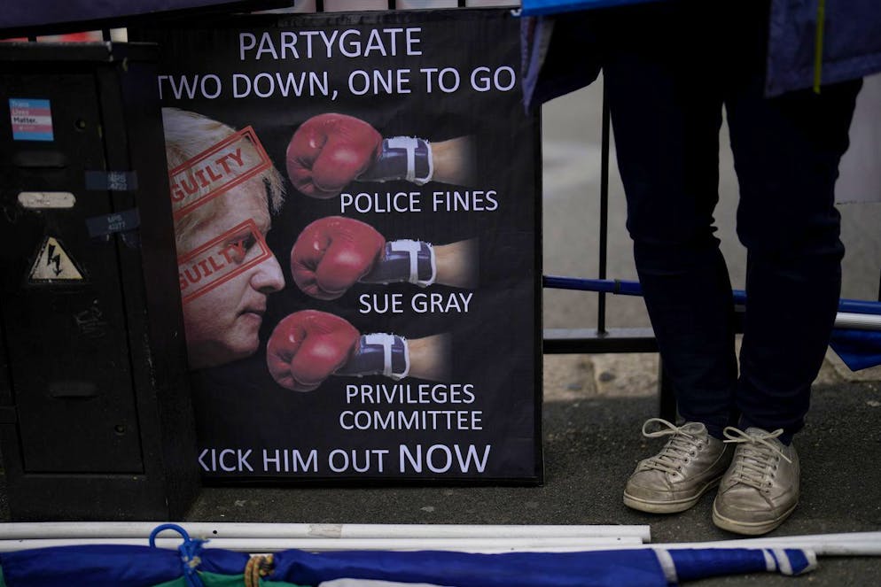 An anti-Boris Johnson, anti-Brexit protester stands next to a placard across the street from the Houses of Parliament on the edge of Parliament Square, in London, Wednesday, May 25, 2022. British Prime Minister Boris Johnson and other senior officials bear responsibility for a culture of rule-breaking that resulted in several parties that breached the U.K.'s COVID-19 lockdown rules, a report into the events said Wednesday. In her report into the 