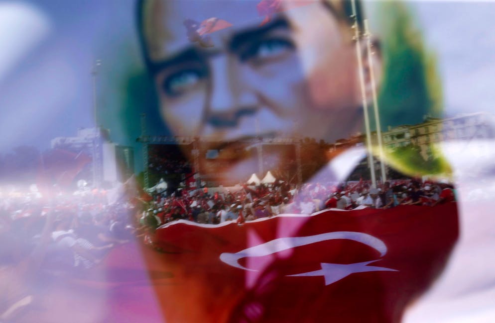epa05439050 A picture taken though a flag with the portrait of Kemal Ataturk, founder of modern Turkey, onto supporters of main opposition Republic Public Party (CHP) hold Turkish flags and pictures of Ataturk, founder of modern Turkey, during a demonstration against coup at Taksim Square, in Istanbul, Turkey, 24 July 2016. Turkish parliament on 21 July formally approved a three-month state of emergency declared by Turkish President Erdogan. The 15 June's failed coup attempt's aftermath was followed by the dismissal of 50,000 workers and the arrest of 8,000 people. At least 290 people were killed and almost 1,500 injured amid violent clashes on 15 July as certain military factions attempted to stage a coup d'etat. The UN and various governments and organizations have urged Turkey to uphold the rule of law and to defend human rights. EPA/SEDAT SUNA