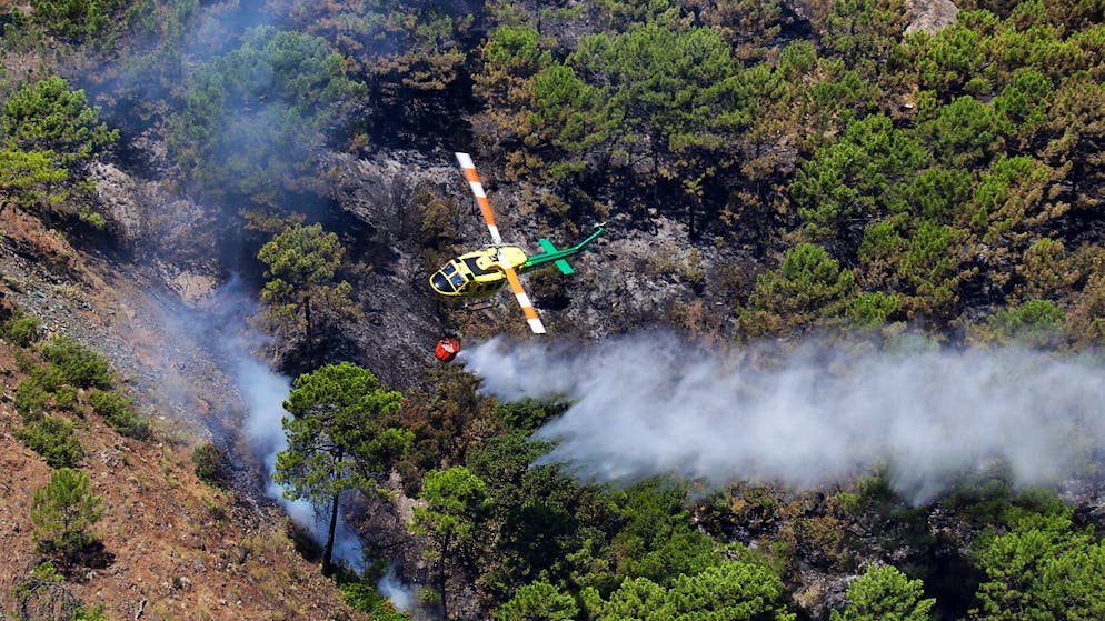 Ein Löschhubschrauber gießt nach einem Waldbrand in der Nähe von Pujerra an der Costa del Sol Wasser über ein verbranntes Gebiet. Foto: Álex Zea/EUROPA PRESS/dpa