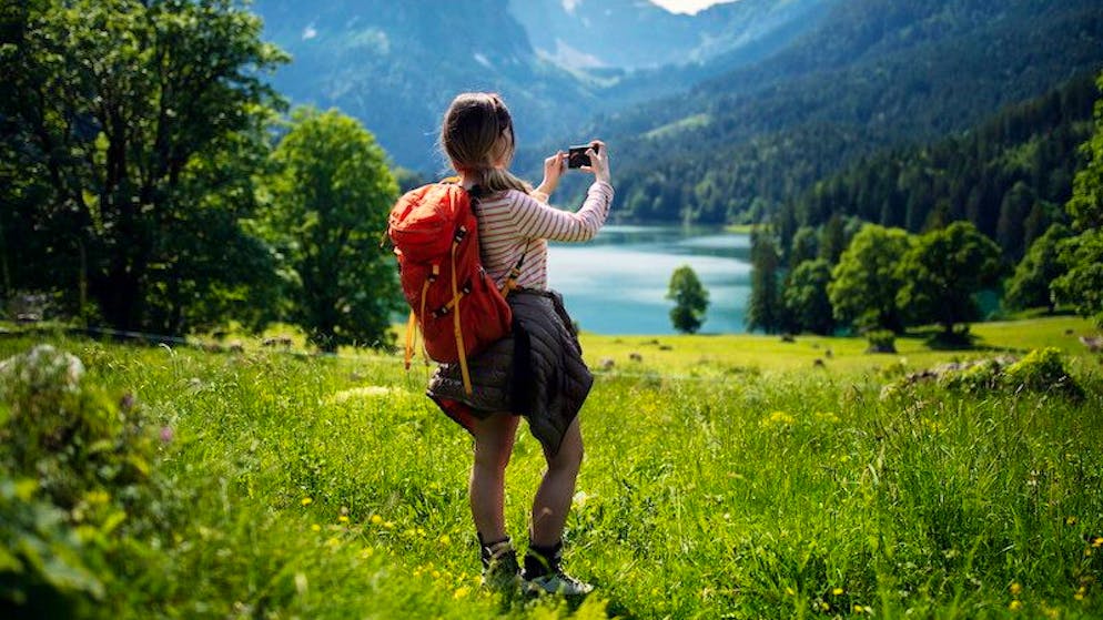 Junge Frau macht ein Foto mit Ihrem Smartphone während einer Wanderung in den Bergen.