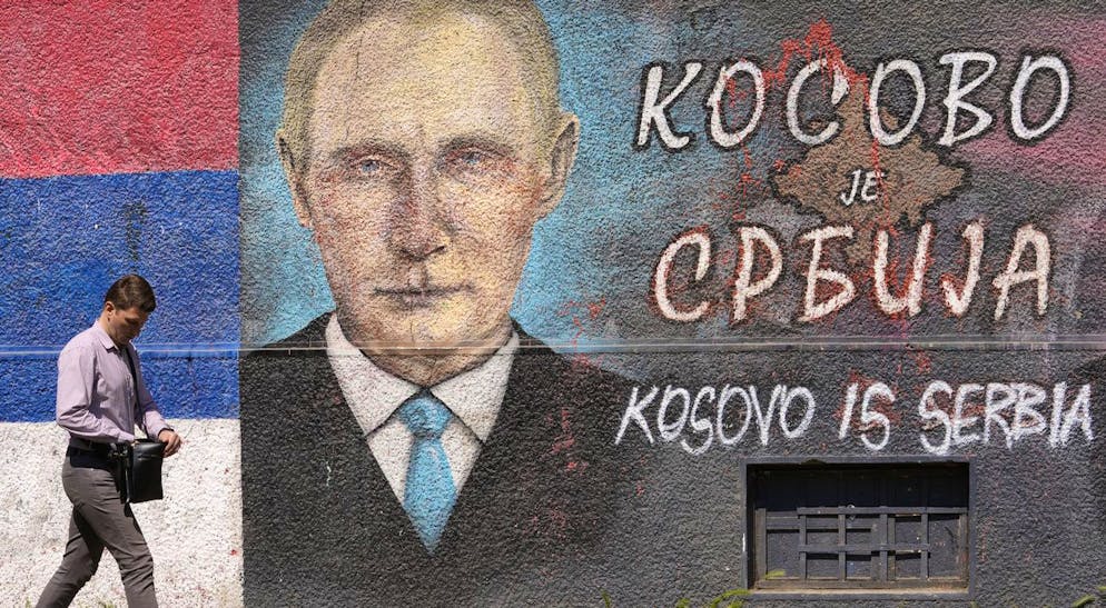 A man walks past a graffiti on a wall depicting the Russian President Vladimir Putin and Serbian flag in Belgrade, Serbia, Friday, May 13, 2022. The Cyrillic letters on graffiti read