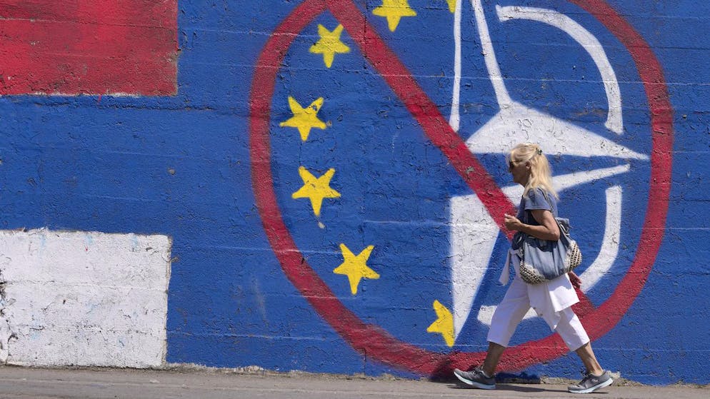 A woman walks by a wall that shows the colours of the Serbian flag and graffiti against EU and NATO in Belgrade, Serbia, Tuesday, June 21, 2022. European Union leaders will seek to offer support this week to six Western Balkan nations that have long been knocking at the bloc's doors, and now see the war in Ukraine raging not far from their borders amid fears that Russia could turn its sights on their region. Serbia, the largest of the six countries, is pivotal in Russia's regional influence. (AP Photo/Darko Vojinovic)