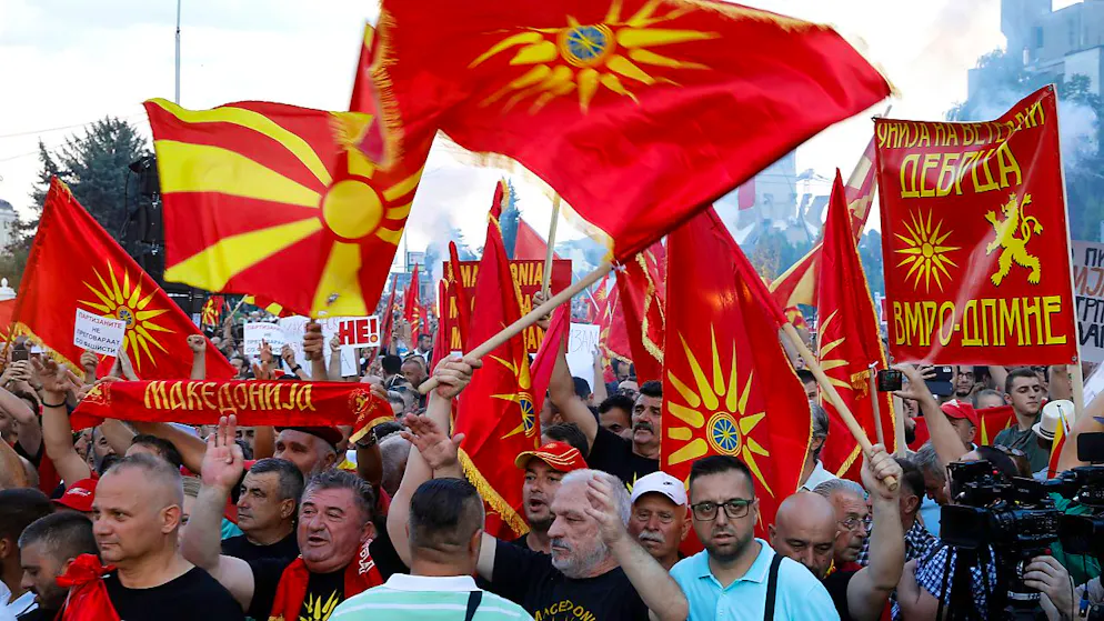 Menschen schwenken in der nordmazedonischen Hauptstadt Skopje die alte und die aktuelle Nationalflagge. Am Samstagabend haben Tausende gegen einen zur Diskussion stehenden Vorschlag zur Beilegung des Streits um Geschichte und nationale Identität mit dem Nachbarland Bulgarien demonstriert. Foto: Boris Grdanoski/AP/dpa