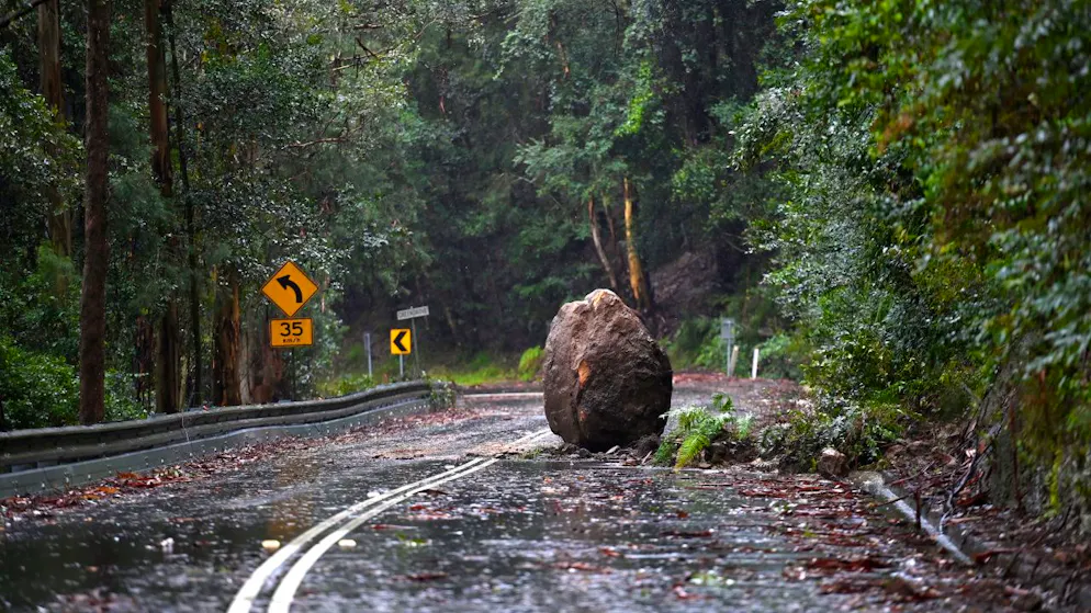 A large boulder blocks Wiseman Ferry Road as torrential rain causes a landslide and floodwaters cut off the road access on Mangrove Mountain,north of Sydney,Tuesday, July 5, 2022. NSW residents are bracing for more heavy rain and flooding as dangerous downpours continue throughout the day.(AAP Image/Jeremy Piper) NO ARCHIVING