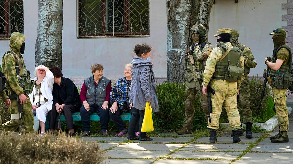 Ältere Anwohner sitzen neben einer Gruppe russischer Soldaten in Cherson. Dieses Foto wurde während einer vom russischen Verteidigungsministerium organisierten Reise aufgenommen.