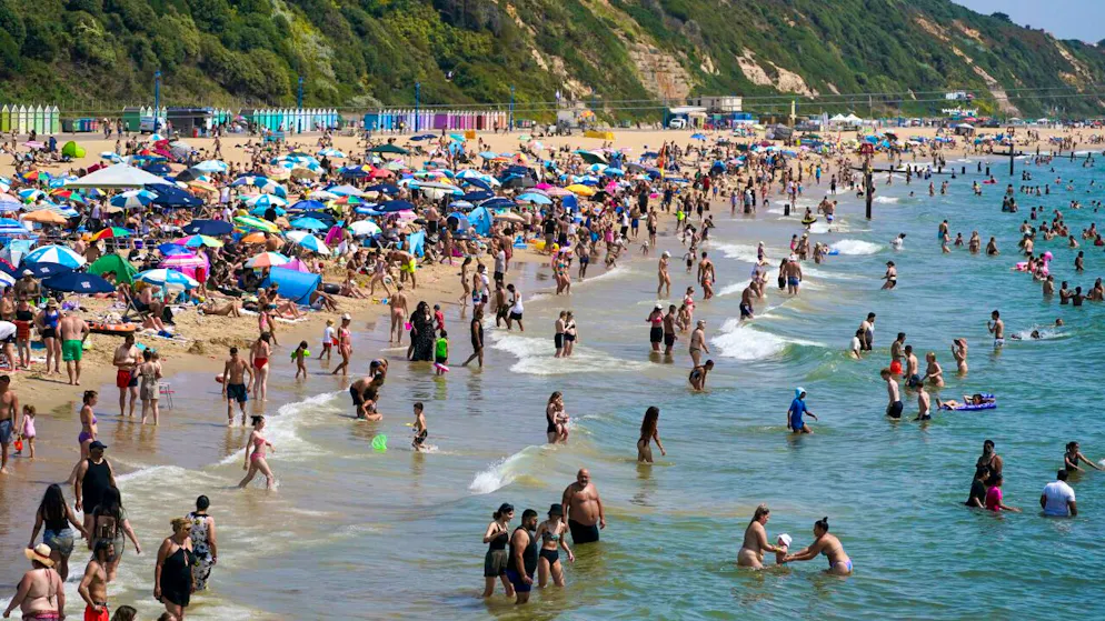 Menschen am Strand in Bournemouth. Ein Mann sucht Schutz unter einem Sonnenschirm am Strand von Bournemouth. Großbritannien hat laut vorläufigen Daten den heißesten Tag seit Beginn der Aufzeichnungen erlebt. Foto: Steve Parsons/PA/AP/dpa
