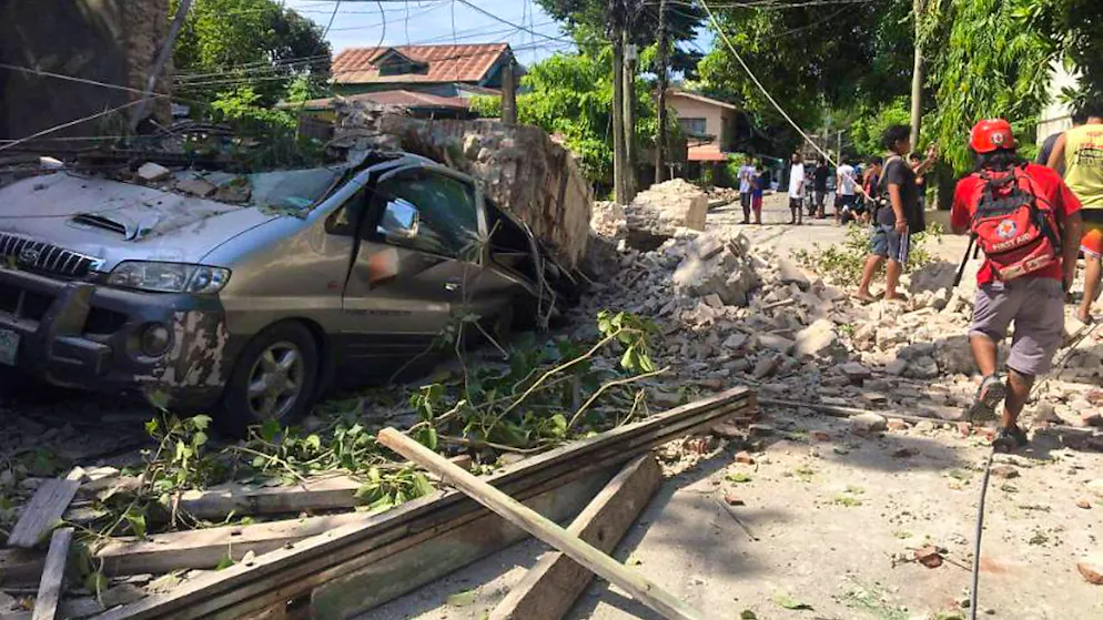HANDOUT - Auf diesem vom philippinischen Roten Kreuz zur Verfügung gestellten Foto steht ein Auto unter Trümmern begraben, nach einem starken Erdbeben in der Provinz Ilocos Sur auf den Philippinen, während Einsatzkräfte des Roten Kreuz und andere Menschen sich ein Überblick der Lage verschaffen. Nach ersten Angaben des Instituts für Vulkanologie und Seismologie der Philippinen (Phivolcs) hatte das Beben eine Stärke von 7,3. Die US-Erdbebenwarte USGS bezifferte die Stärke auf 7,1. Das Epizentrum befand sich in dem Ort Lagangilang in der Provinz Abra. Foto: Uncredited/PHILIPPINE RED CROSS/AP/dpa - ACHTUNG: Nur zur redaktionellen Verwendung und nur mit vollständiger Nennung des vorstehenden Credits