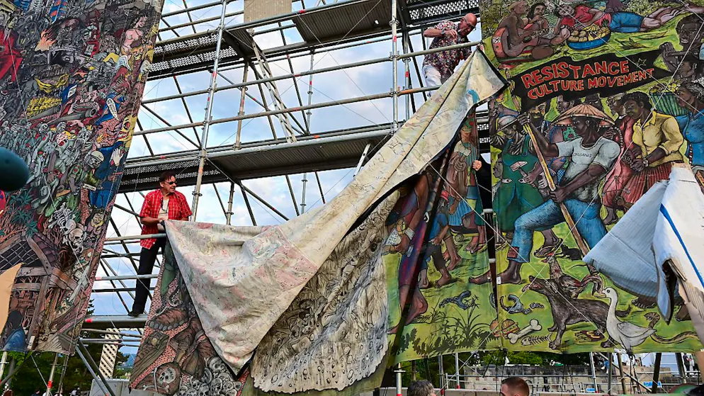 Documenta-Mitarbeiter bauen das umstrittene Großbanner «People's Justice» des indonesischen Künstlerkollektivs Taring Padi auf dem Friedrichsplatz ab. Foto: Uwe Zucchi/dpa - ACHTUNG: Nur zur redaktionellen Verwendung im Zusammenhang mit einer Berichterstattung über die documenta 15 und nur mit vollständiger Nennung des vorstehenden Credits