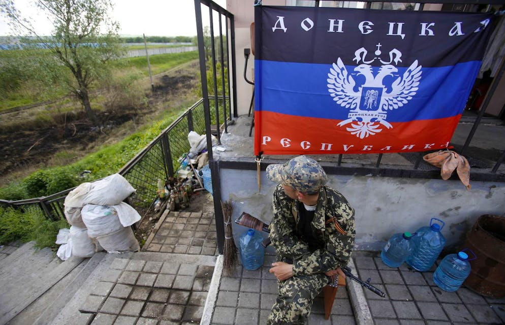 An armed pro-Russian man sits beneath a flag of the Donetsk People's Republic at a barricade on the road to the city of Sloviansk in eastern Ukraine, Sunday, May 11, 2014.  Russian opposition votes in controversial and hastily organized independence referendum.  Sunday's ballots sought approval to declare themselves as sovereign people's republics in Donetsk and Luhansk regions, where rebels have seized government buildings and clashed with police and Ukrainian troops.  (AP Photo/Darko Vojinovic)