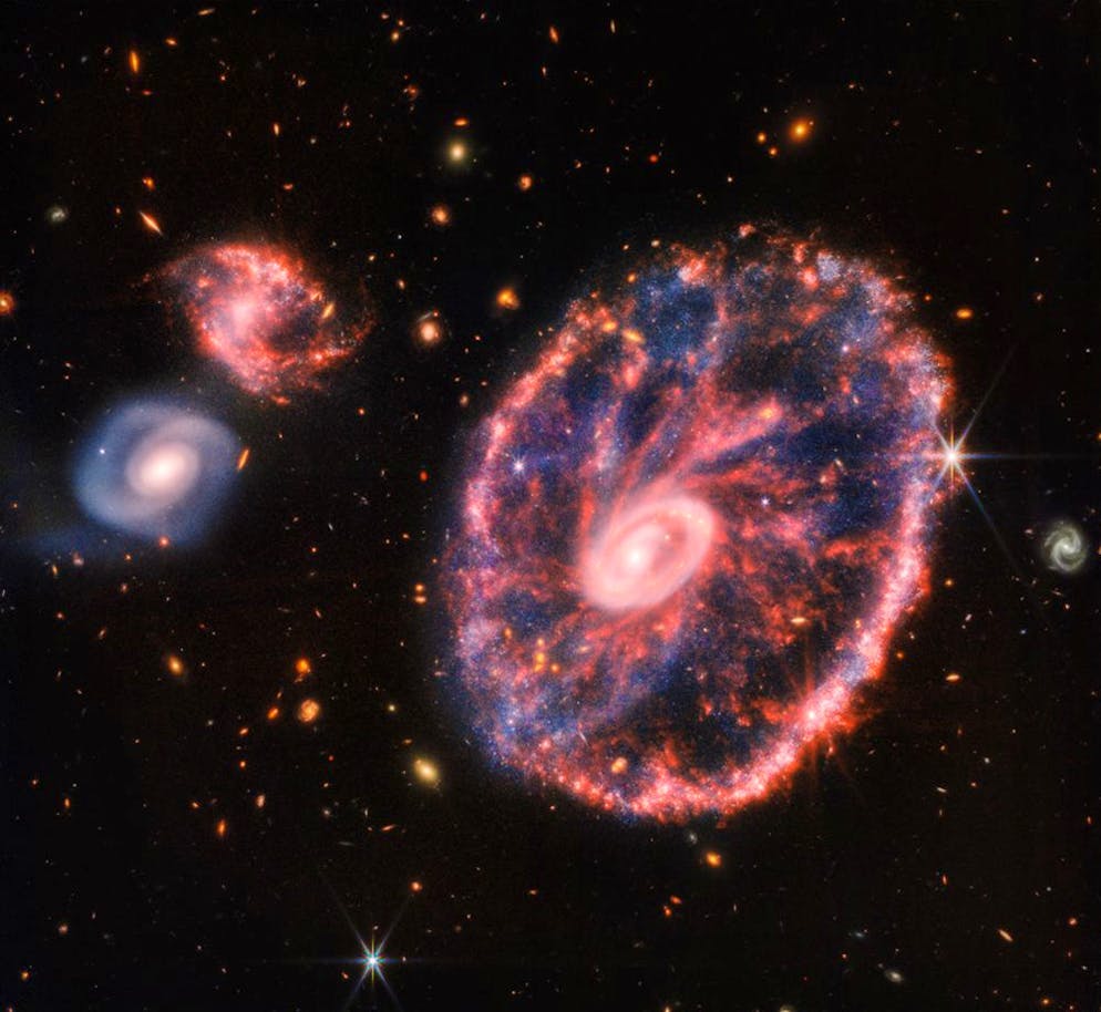 Ecco le spettacolari foto del telescopio spaziale Webb. Questa è la «Cartwheel Galaxy», cioè la galassia ruota di carro. Da 400 milioni di anni qui si sono scontrate le galassie. Nell'anello chiaro e interno si vede che la galassia spiraliforme si è conservata. La polvere rosso brillante dagli idrocarburi crea le sorgenti striature.