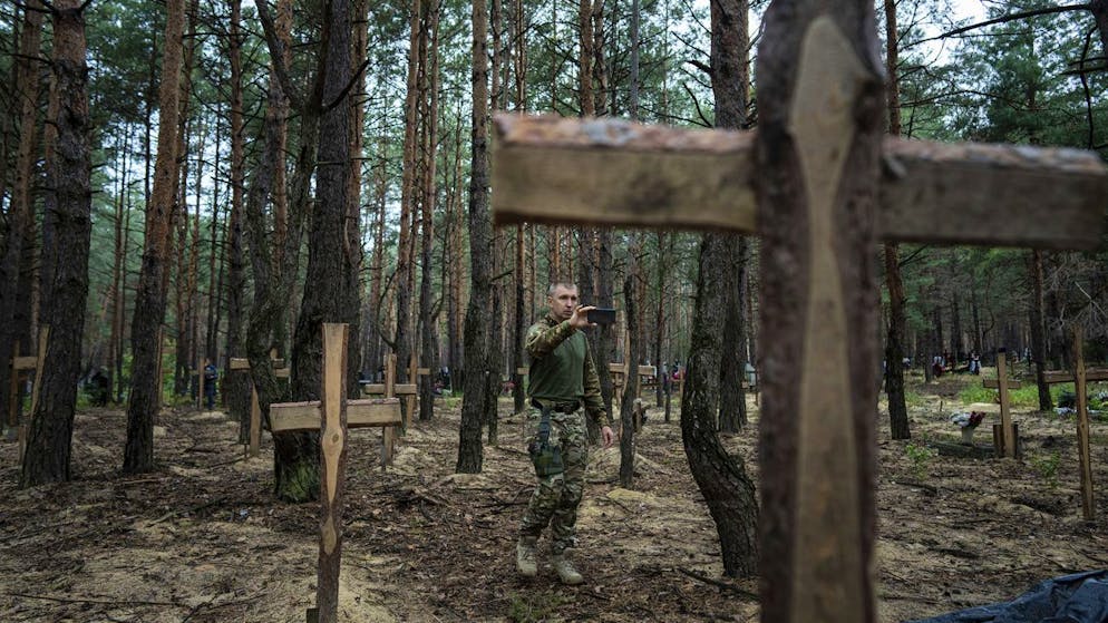 Oleg Kotenko, Commissioner for the Affairs of Missing Persons under Special Circumstances, uses his smartphone to photograph unidentified graves of unidentified civilians and Ukrainian soldiers killed by Russian forces in the Izium region of Ukraine, Thursday, Sept. 15, 2022.  Near the start of the war.  A mass grave of Ukrainian soldiers and civilians with unknown burials was discovered in the forest of the recently recovered city of Isium.  (AP Photo/Evgeniy Maloletka)