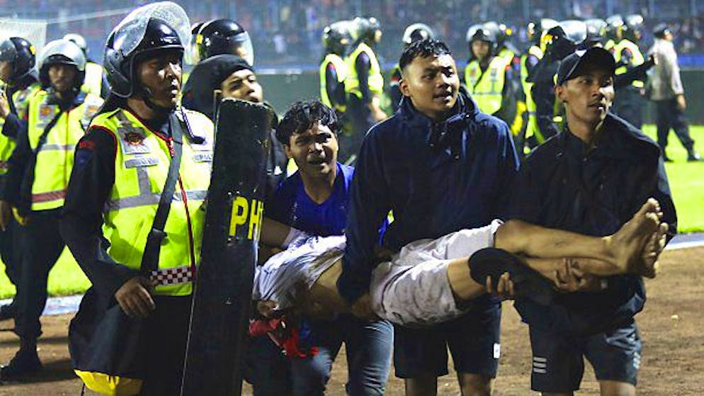 Penggemar sepak bola membawa seorang pria yang terluka keluar lapangan.