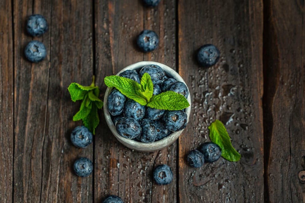 Ripe juicy blueberries  with mint leaves and water droplets on a wooden table. Healthy eating, vegetarian concept,  rustic style, top view.