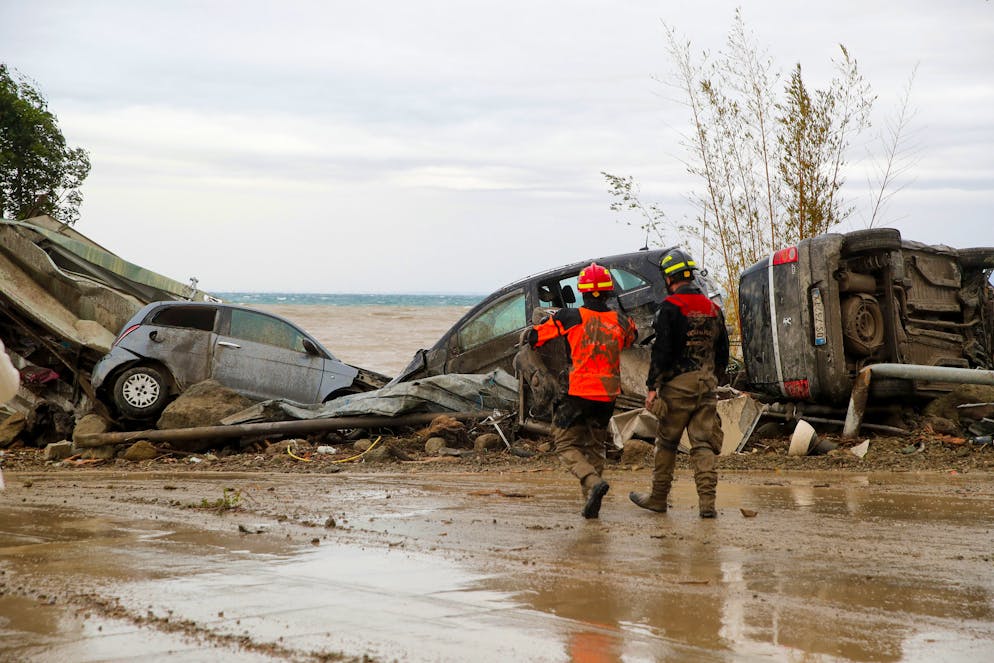 Rescuers walk past damaged vehicles after heavy rainfall triggered landslides that collapsed buildings and left as many as 12 people missing, in Casamicciola, on the southern Italian island of Ischia, Saturday, Nov. 26, 2022. Firefighters are working on rescue efforts as reinforcements are being sent from nearby Naples, but are encountering difficulties in reaching the island either by motorboat or helicopter due to the weather. (AP Photo/Salvatore Laporta)