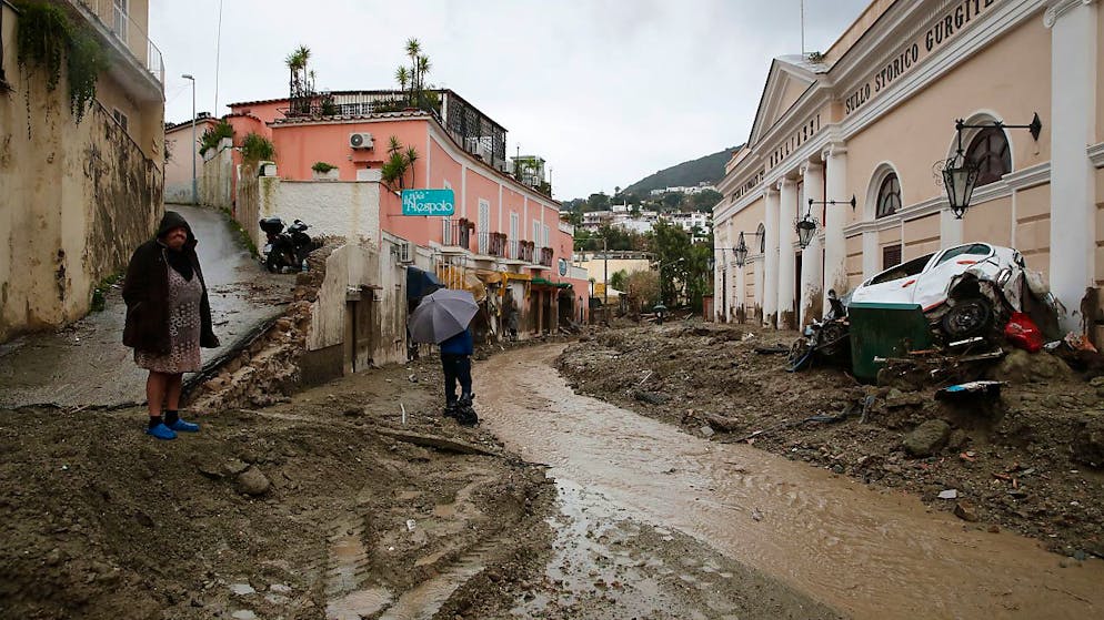 Menschen stehen an einer mit Schlamm und Wasser bedeckten Strasse, nachdem schwere Regenfälle Erdrutsche ausgelöst hatten.