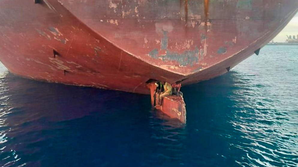 Drei Männer sitzen an einer ungewöhnlichen und gefährlichen Stelle eines Öltankers, der in einem Hafen der Kanarischen Inseln vor Anker liegt.