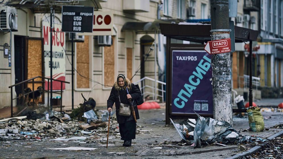 dpatopbilder - Eine ältere Anwohnerin geht mit ihren Gehstock eintlang beschädigter Gebäude. Foto: Libkos/AP/dpa