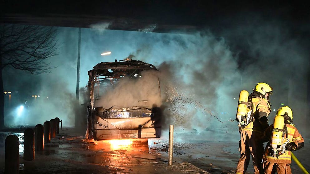 Feuerwehrmänner löschen einen Reisebus, der von Unbekannten angezündet worden war. Foto: Paul Zinken/dpa