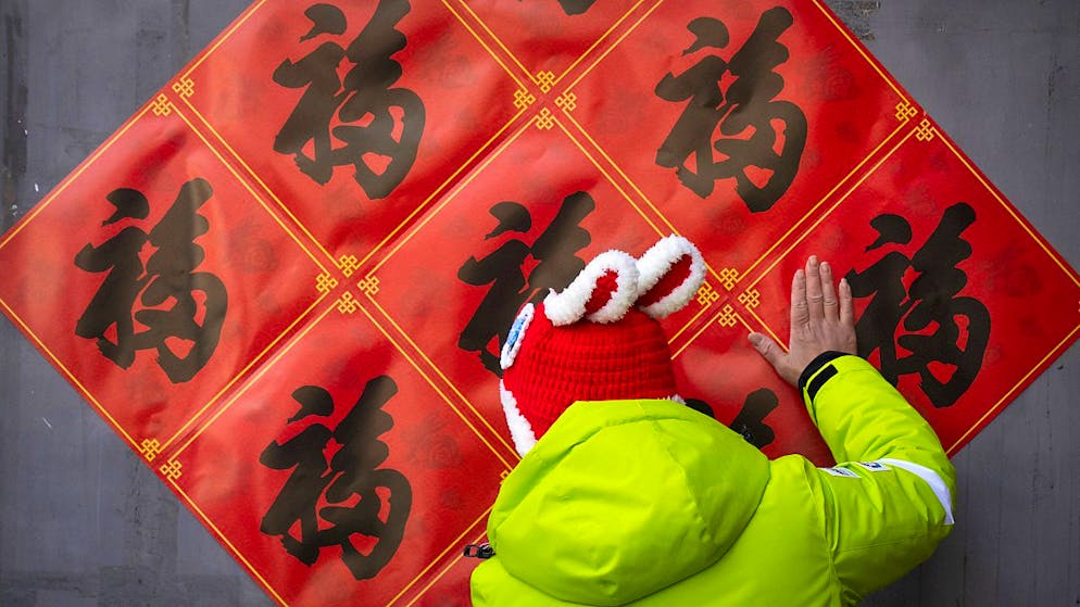Eine Frau in Peking glättet mit ihrer Hand die Dekoration für das bevorstehende Mondneujahr. Foto: Mark Schiefelbein/AP/dpa