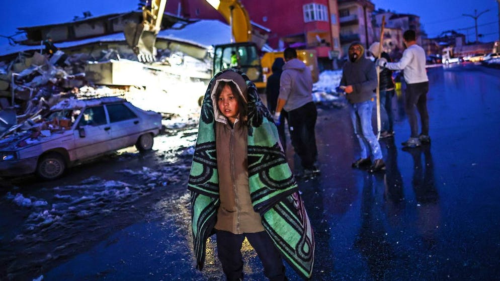 Erdbeben in der Türkei und in Syrien. <strong>7. Februar, Türkei:</strong> Angehörige von Vermissten warten bei Minustemperaturen vor einem eingestürzten Gebäude, während Rettungskräfte im Bezirk Elbistan in Kahramanmaras nach Überlebenden suchen. 
